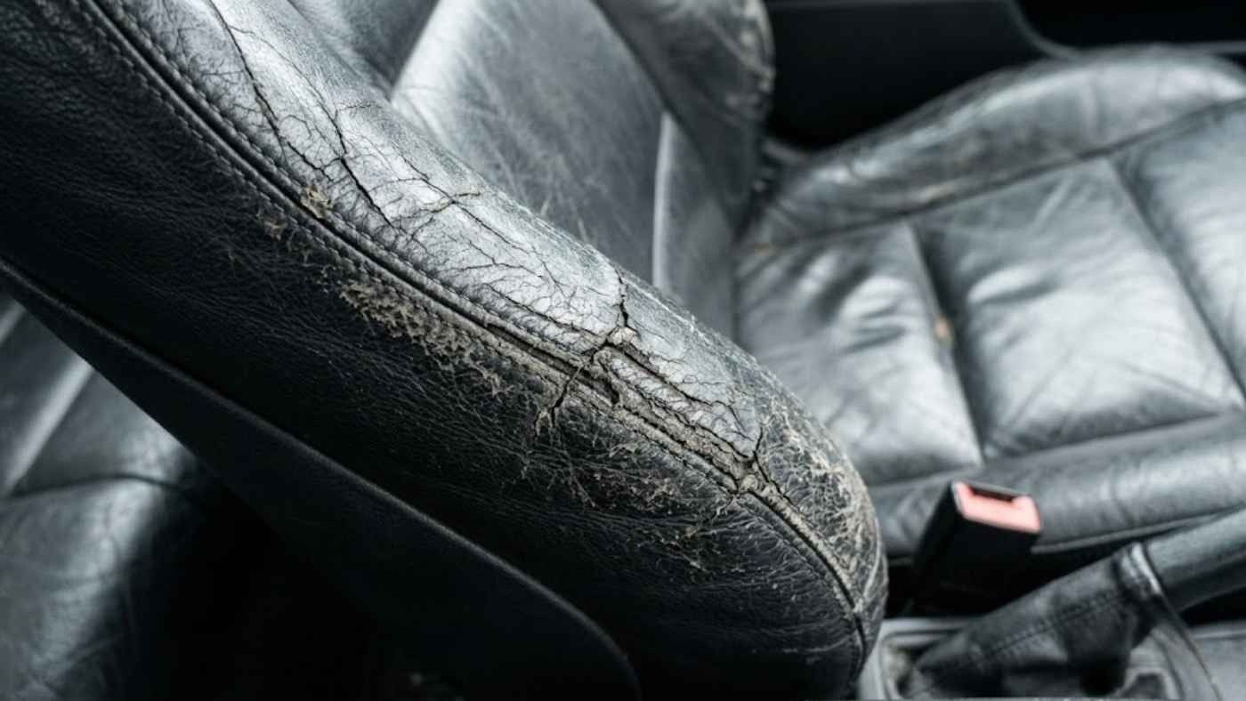 Cracked leather driver-seat bolster showing severe wear, highlighting costly upholstery damage without seat covers.